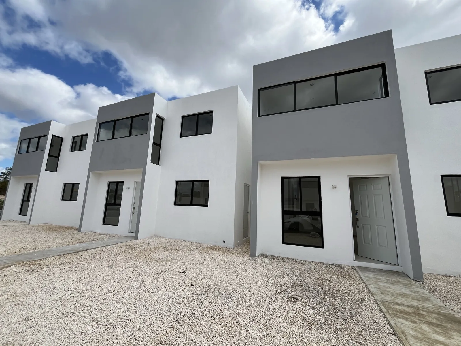 Fachada de la casa nueva de dos plantas en Ciudad Caucel, en volúmenes blancos y grises con ventanales de marco negro