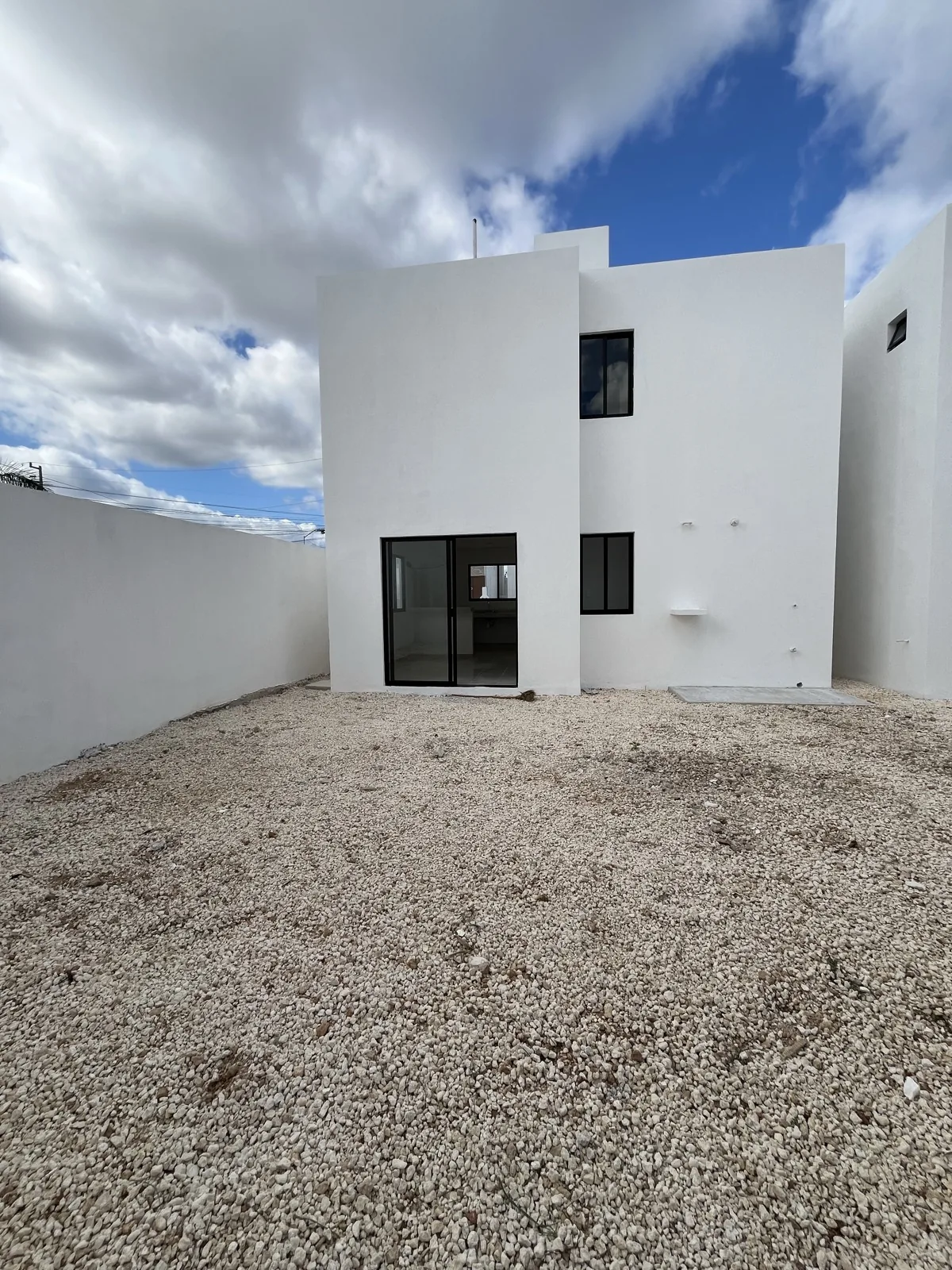 Patio trasero de la casa con muro perimetral y la fachada posterior de dos plantas