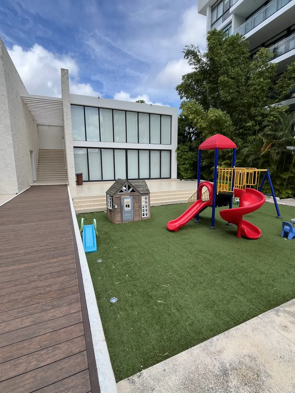 Área de juegos infantiles con resbaladilla y casita sobre pasto sintético