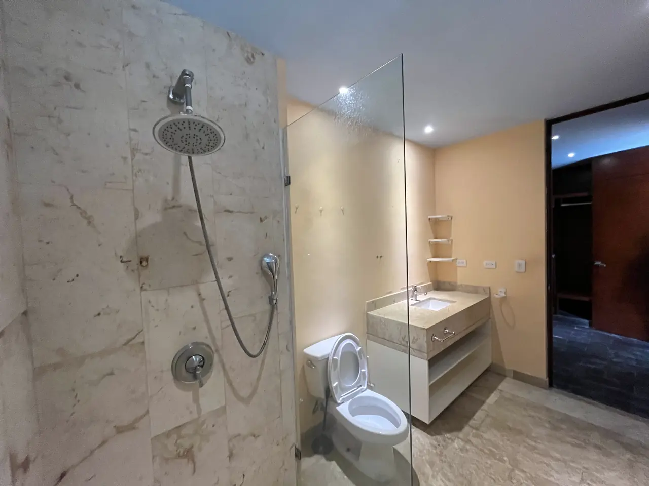 Baño principal con regadera de mármol beige, cancel de vidrio y lavabo de cubierta de piedra