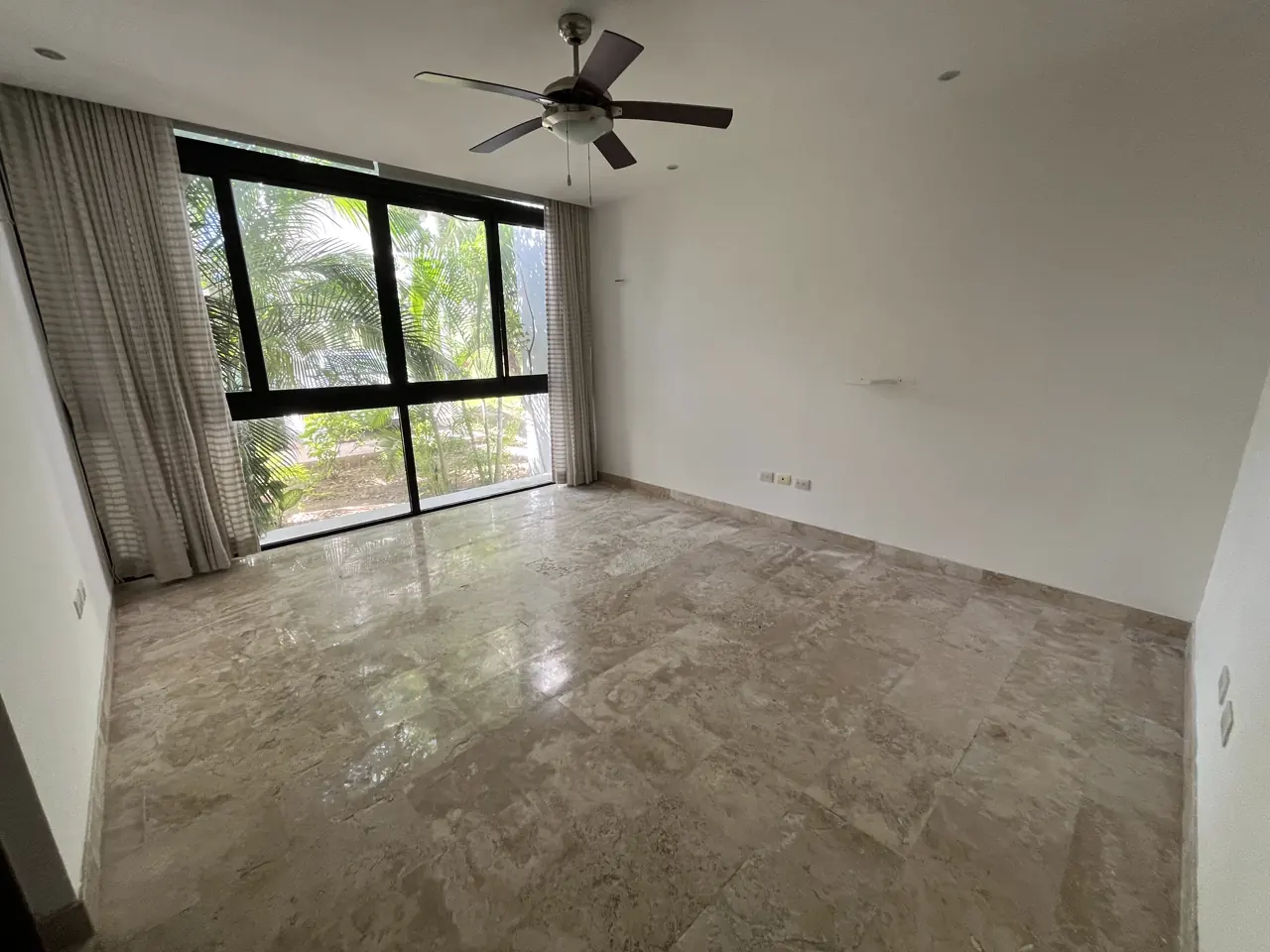 Recámara principal con ventanal de piso a techo, cortina y ventilador de techo